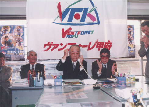 Ｊリーグ加盟承認決定の電話連絡を受け、拳を握り上げる深澤孟雄ヴァンフォーレ山梨スポーツクラブ初代社長。右隣で拍手するのは鈴木旻チームオーナー